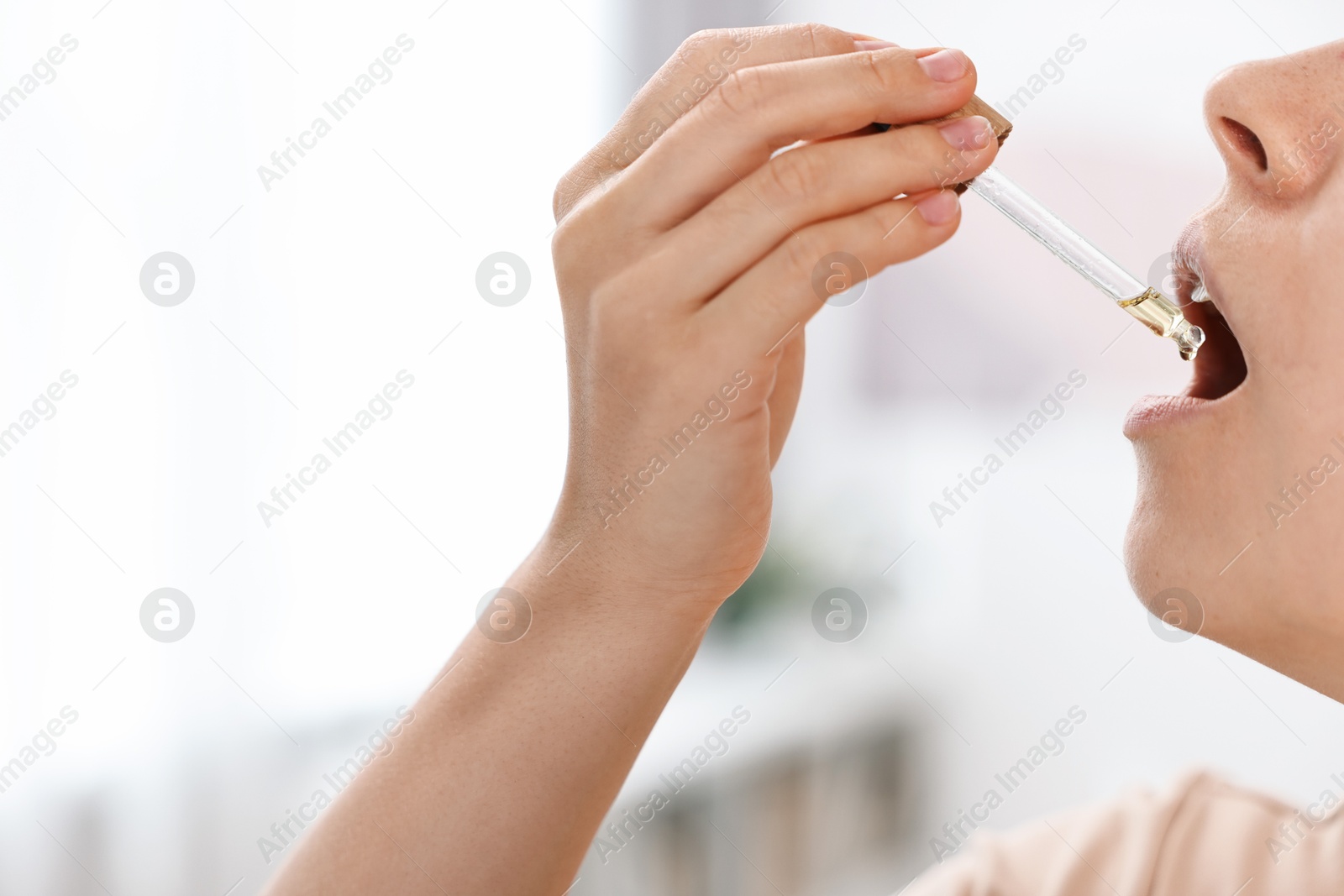 Photo of Young woman taking CBD tincture indoors, closeup. Space for text