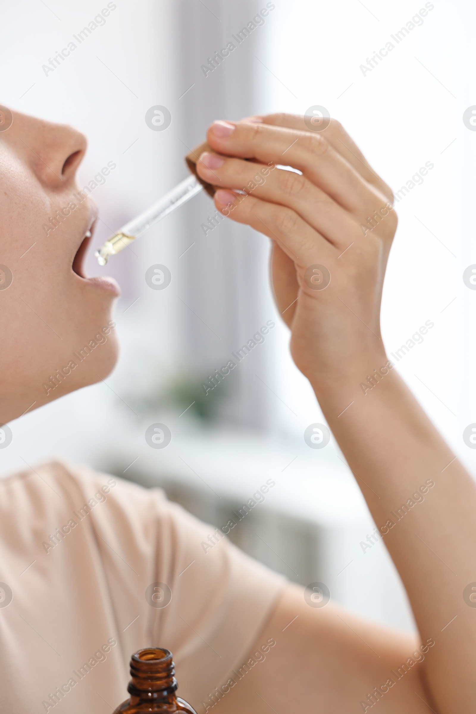 Photo of Young woman taking CBD tincture indoors, closeup