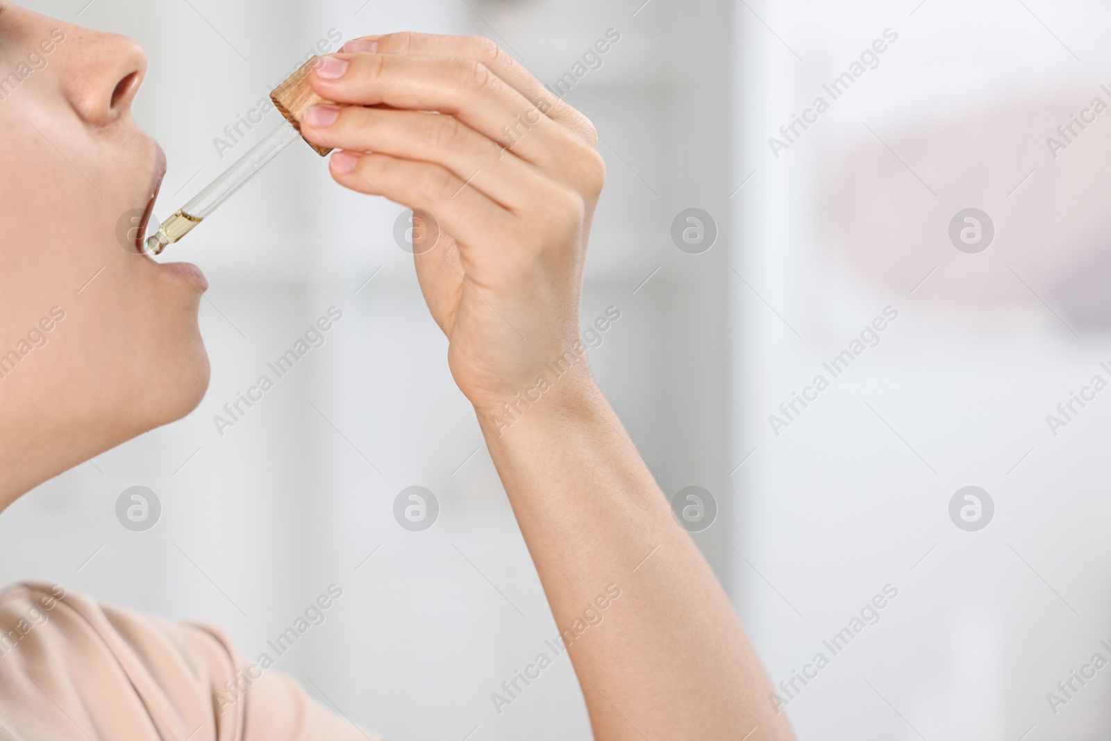 Photo of Young woman taking CBD tincture indoors, closeup. Space for text