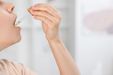 Photo of Young woman taking CBD tincture indoors, closeup. Space for text