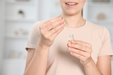 Photo of Young woman taking CBD tincture indoors, closeup