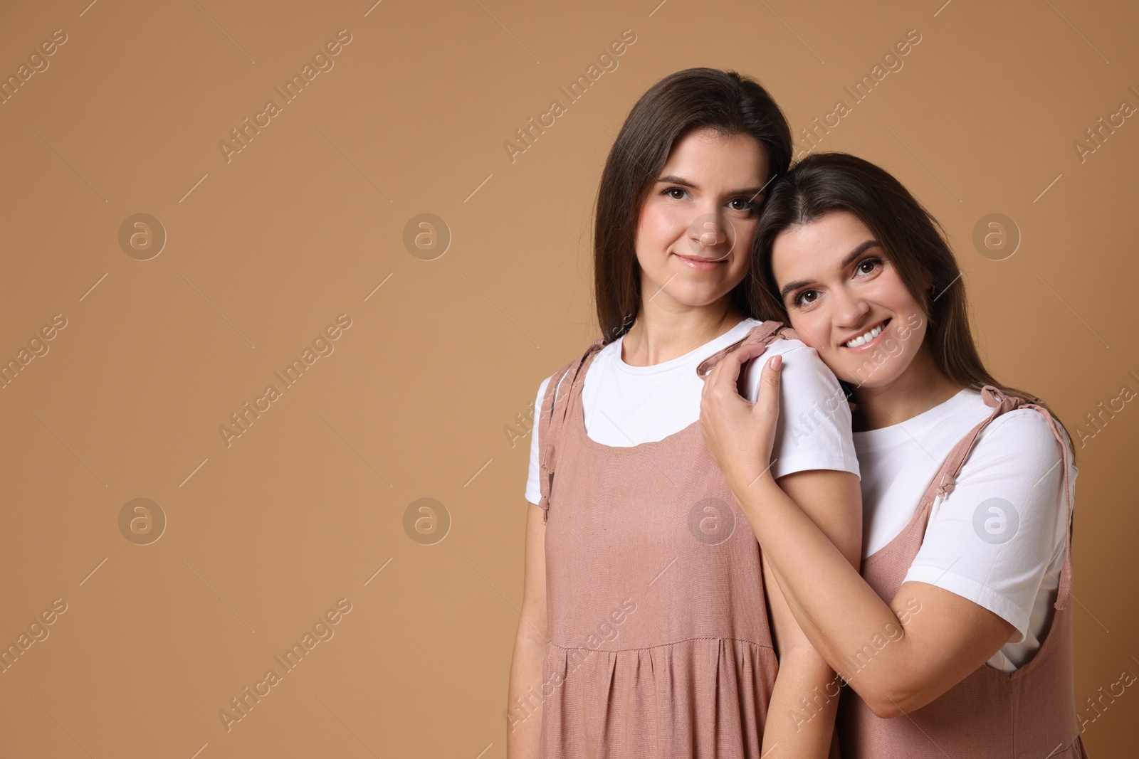 Photo of Portrait of happy twin sisters on pale brown background, space for text