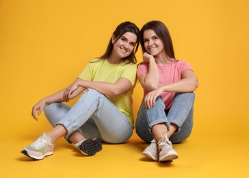 Portrait of happy twin sisters on orange background