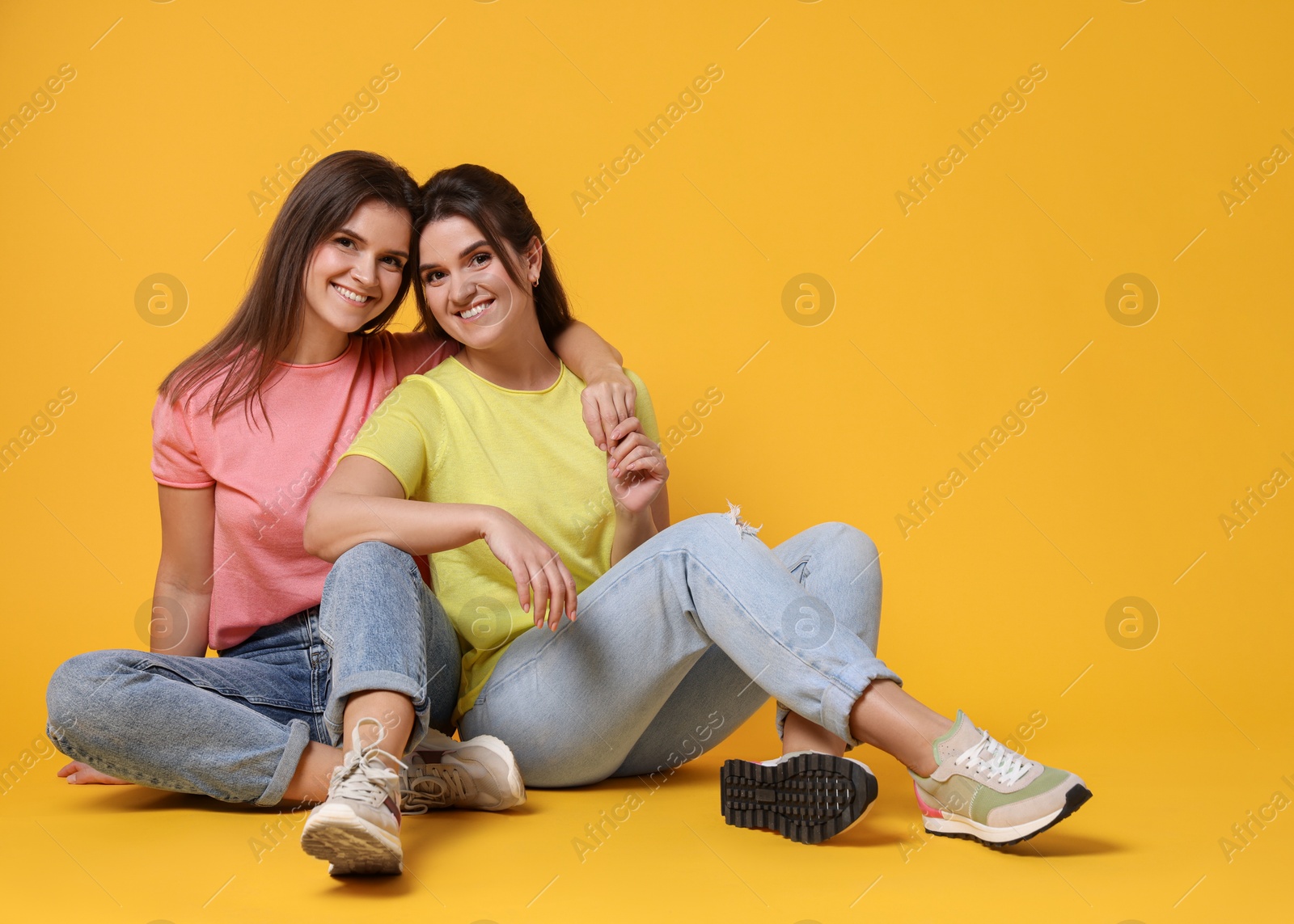 Photo of Portrait of happy twin sisters on orange background, space for text