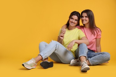 Photo of Portrait of happy twin sisters on orange background, space for text