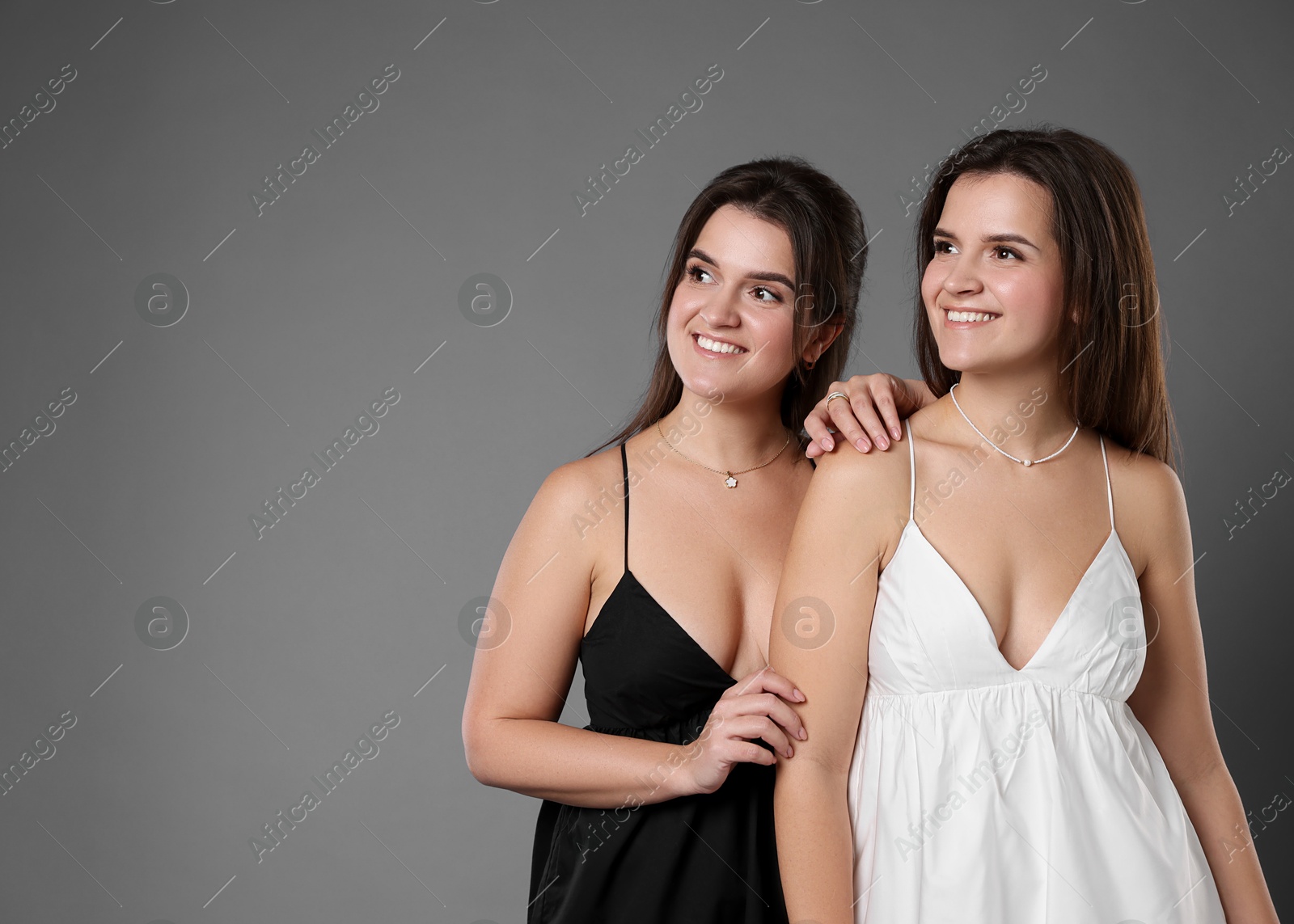 Photo of Portrait of beautiful twin sisters on grey background, space for text