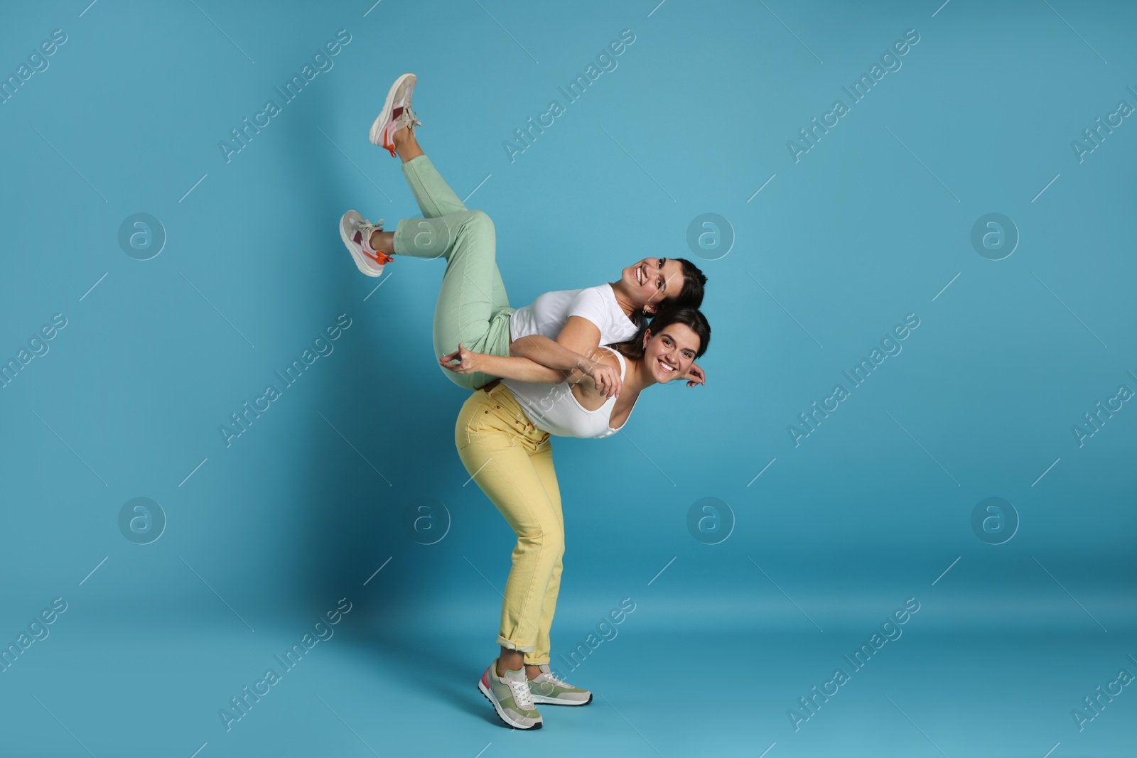 Photo of Beautiful twin sisters having fun on light blue background