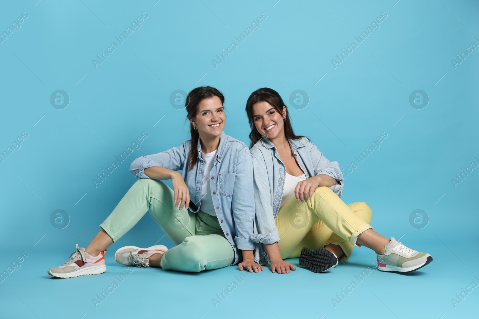 Photo of Portrait of beautiful twin sisters on light blue background