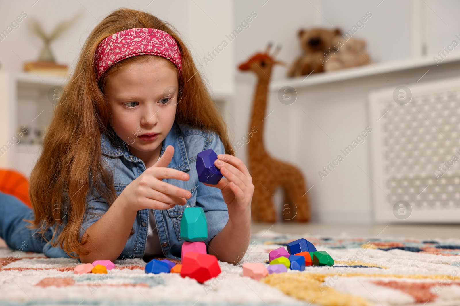 Photo of Little girl building tower with balancing stones on floor indoors, space for text