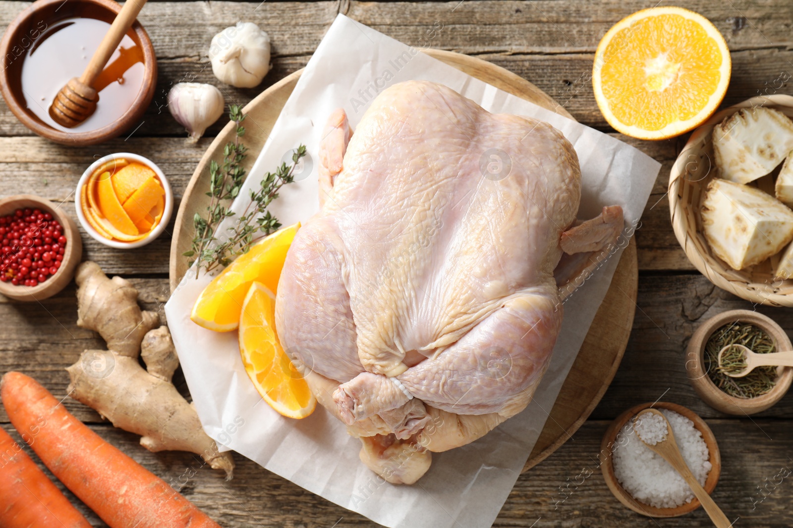 Photo of Uncooked turkey, orange slices, carrots and spices on wooden table, flat lay