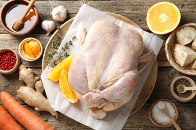 Photo of Uncooked turkey, orange slices, carrots and spices on wooden table, flat lay