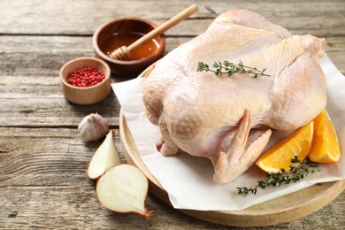 Photo of Uncooked turkey, orange slices and spices on wooden table, closeup