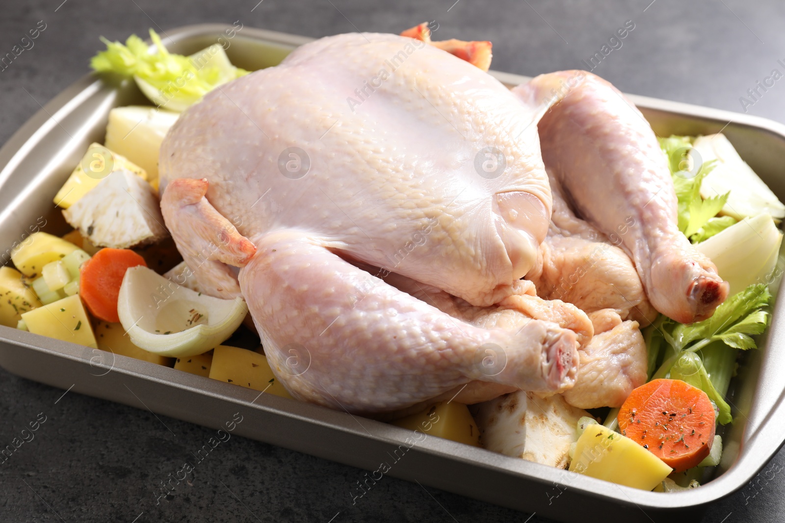 Photo of Raw turkey and vegetables in baking dish on grey table, closeup