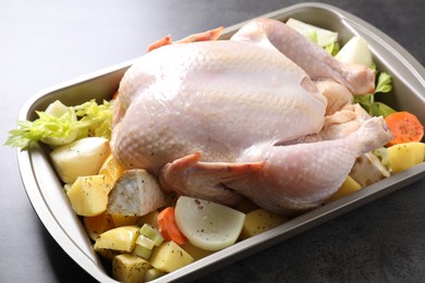 Raw turkey and vegetables in baking dish on grey table, closeup