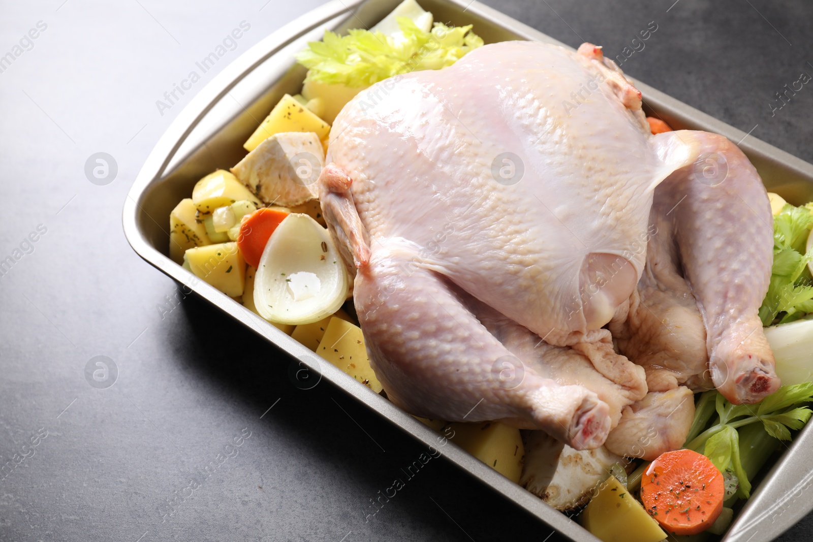 Photo of Raw turkey and vegetables in baking dish on grey table, closeup