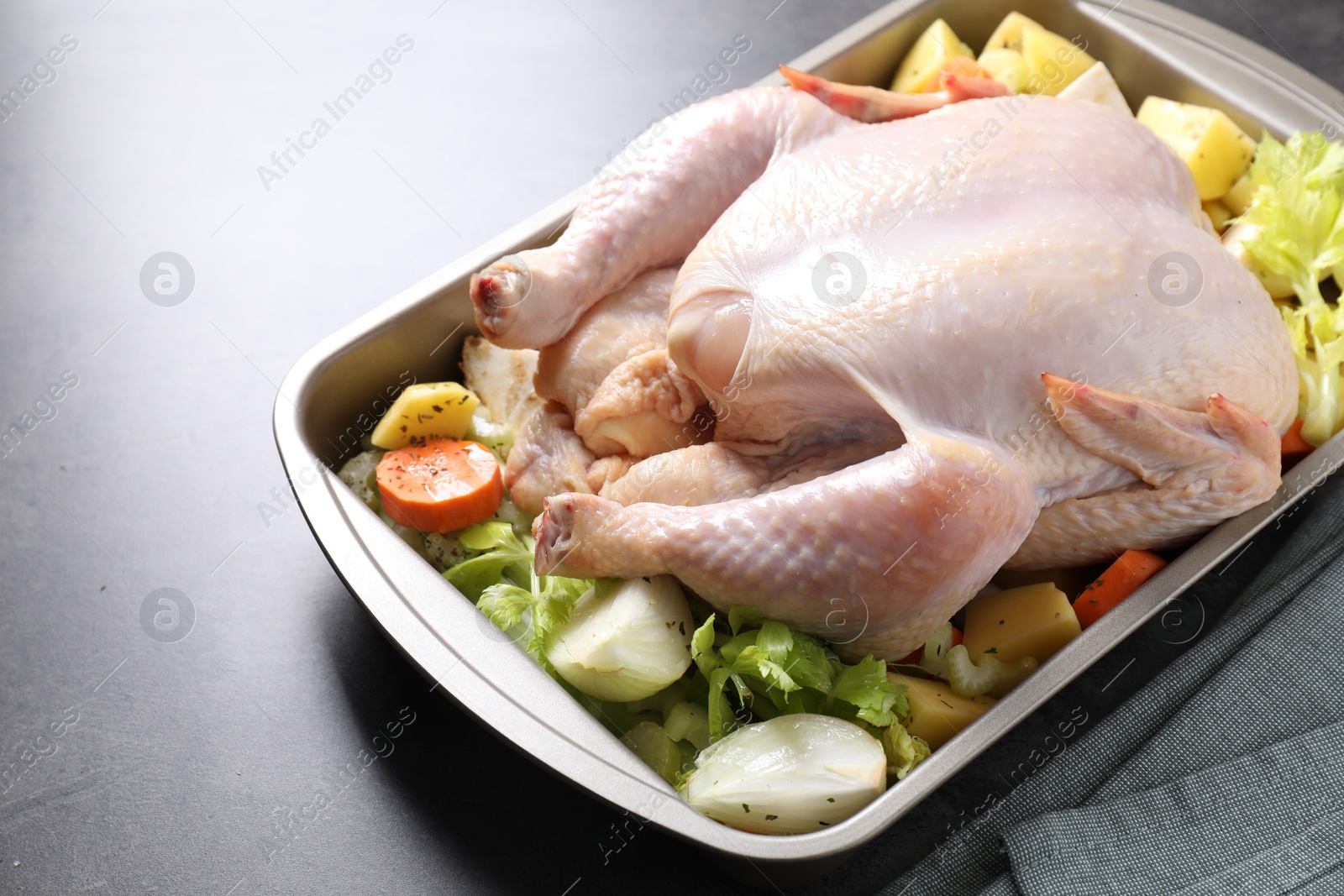 Photo of Raw turkey and vegetables in baking dish on grey table, closeup