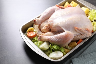 Photo of Raw turkey and vegetables in baking dish on grey table, closeup