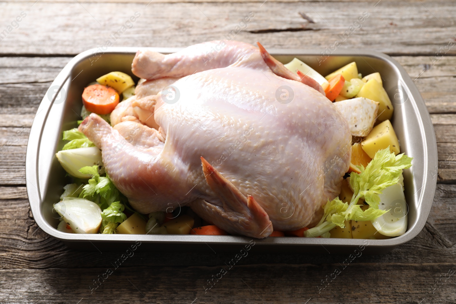 Photo of Raw turkey and vegetables in baking dish on wooden table, closeup