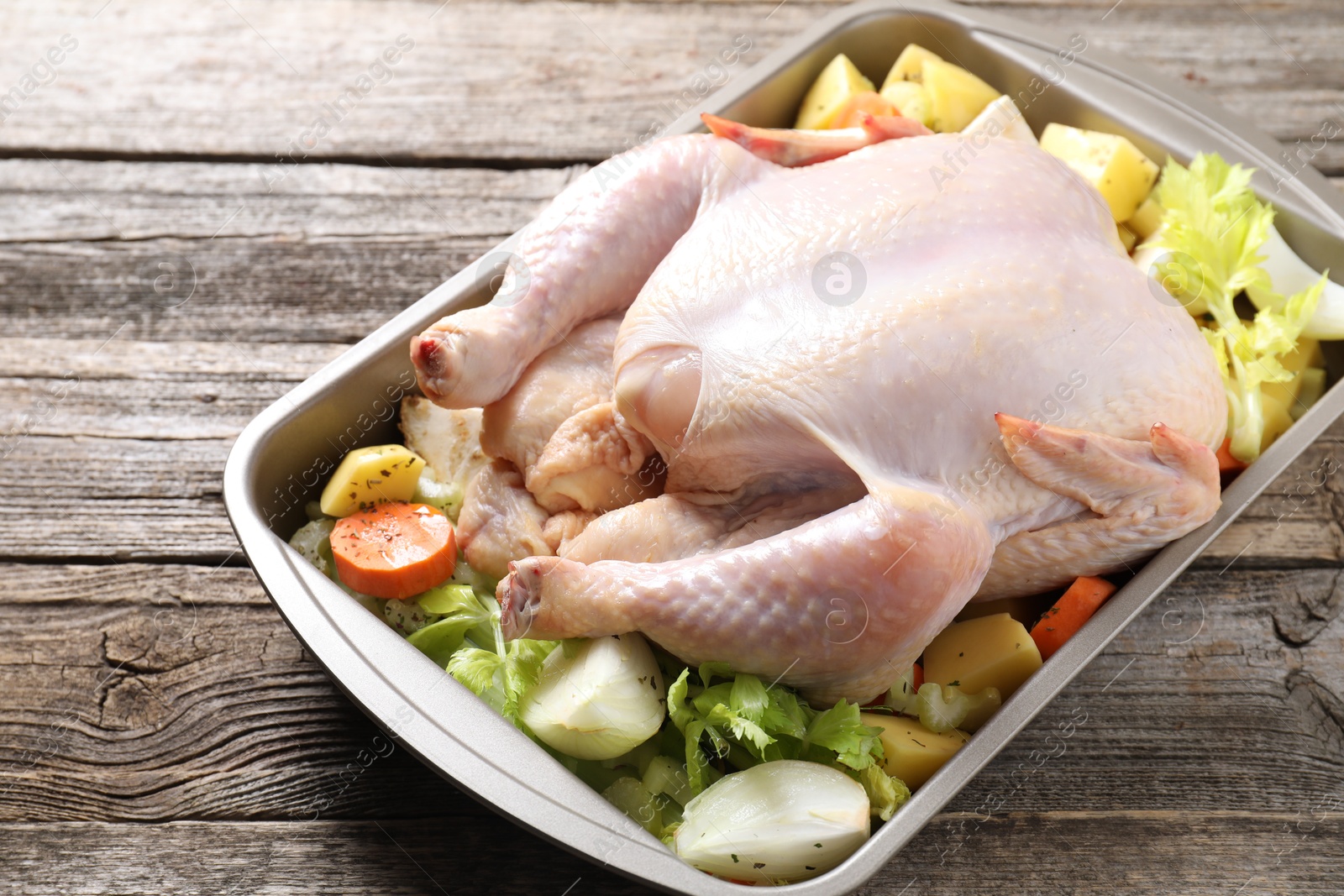 Photo of Raw turkey and vegetables in baking dish on wooden table, closeup