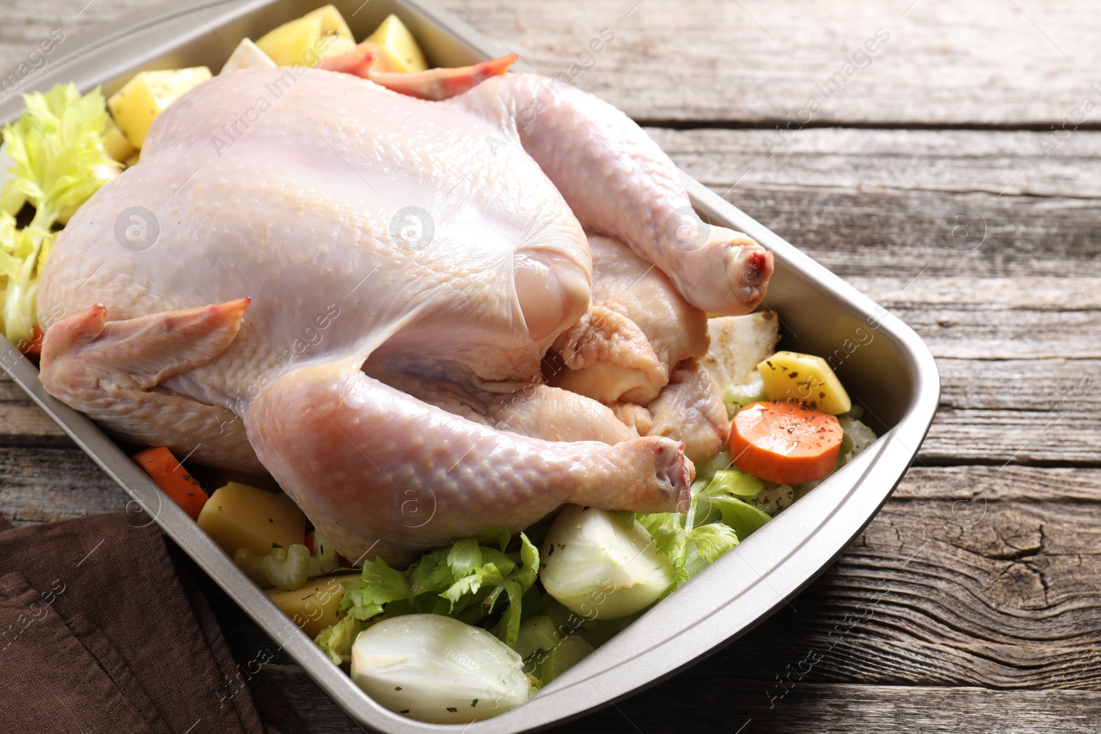 Photo of Raw turkey and vegetables in baking dish on wooden table, closeup