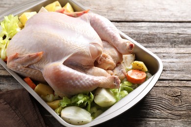 Photo of Raw turkey and vegetables in baking dish on wooden table, closeup