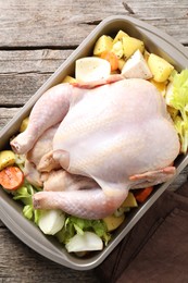 Photo of Raw turkey and vegetables in baking dish on wooden table, top view