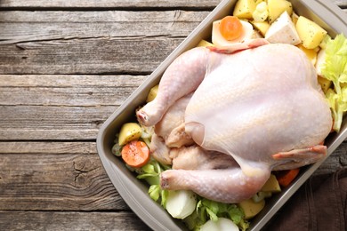 Photo of Raw turkey and vegetables in baking dish on wooden table, top view. Space for text