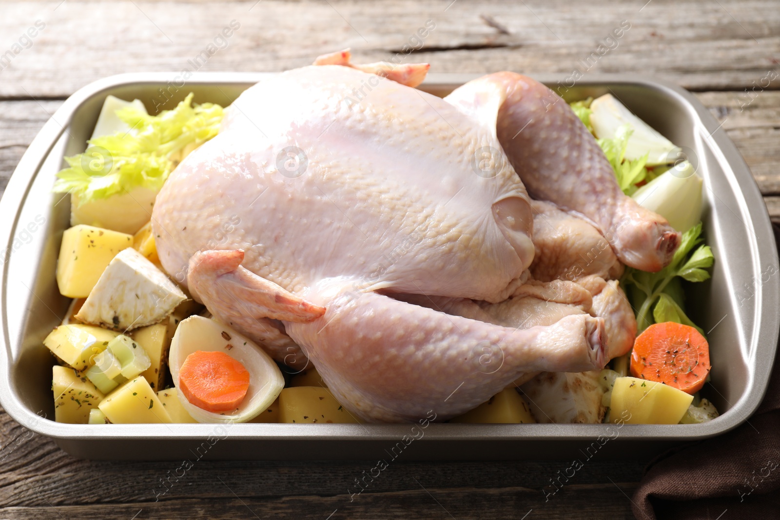 Photo of Raw turkey and vegetables in baking dish on wooden table, closeup