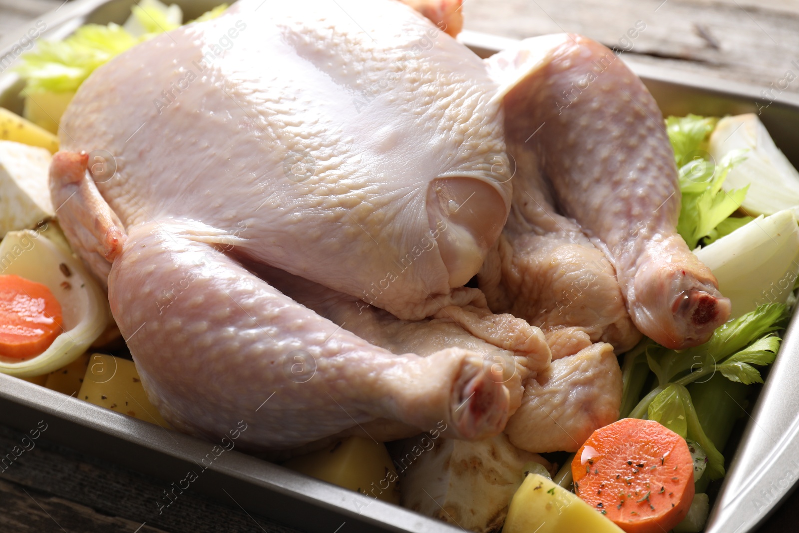 Photo of Raw turkey and vegetables in baking dish on wooden table, closeup