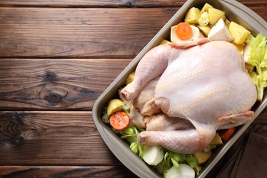 Photo of Raw turkey and vegetables in baking dish on wooden table, top view. Space for text