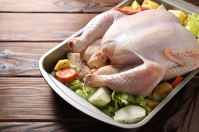 Photo of Raw turkey and vegetables in baking dish on wooden table, closeup