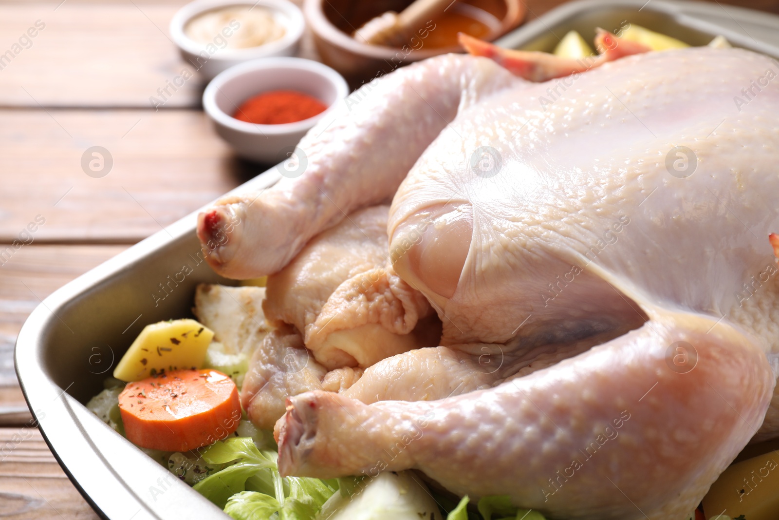 Photo of Raw turkey with different vegetables and spices on wooden table, closeup