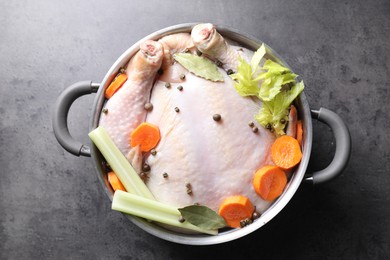 Photo of Whole raw turkey, cut carrot, celery and spices in pot on grey textured table, top view