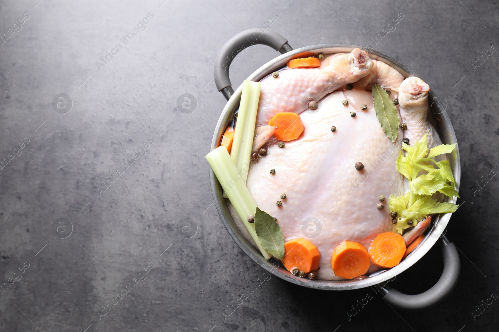 Photo of Whole raw turkey, cut carrot, celery and spices in pot on grey textured table, top view. Space for text