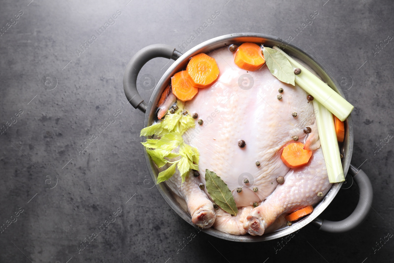 Photo of Whole raw turkey, cut carrot, celery and spices in pot on grey textured table, top view. Space for text