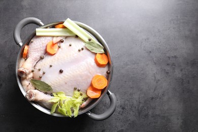 Photo of Whole raw turkey, cut carrot, celery and spices in pot on grey textured table, top view. Space for text