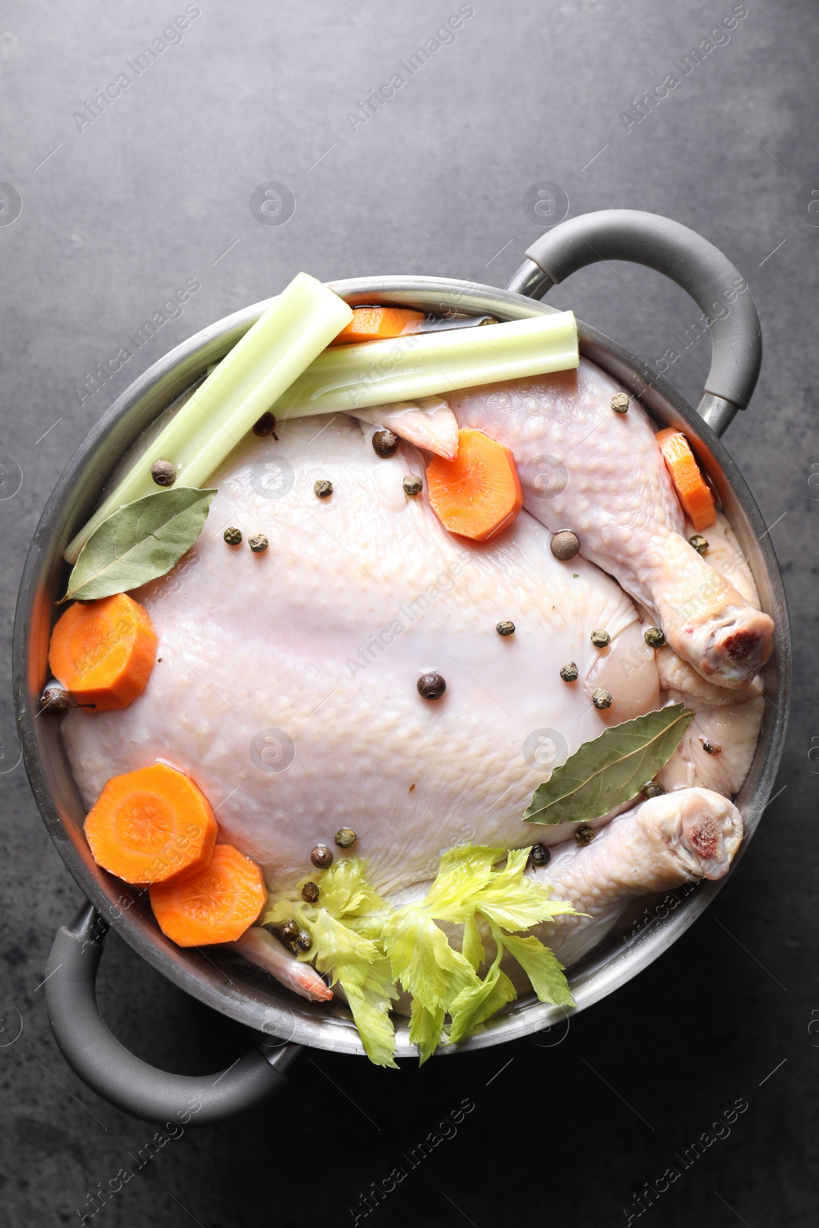 Photo of Whole raw turkey, cut carrot, celery and spices in pot on grey textured table, top view