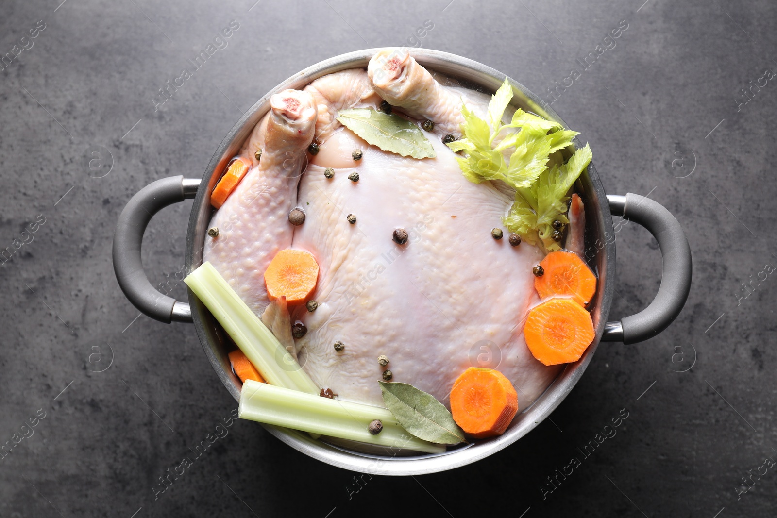 Photo of Whole raw turkey, cut carrot, celery and spices in pot on grey textured table, top view