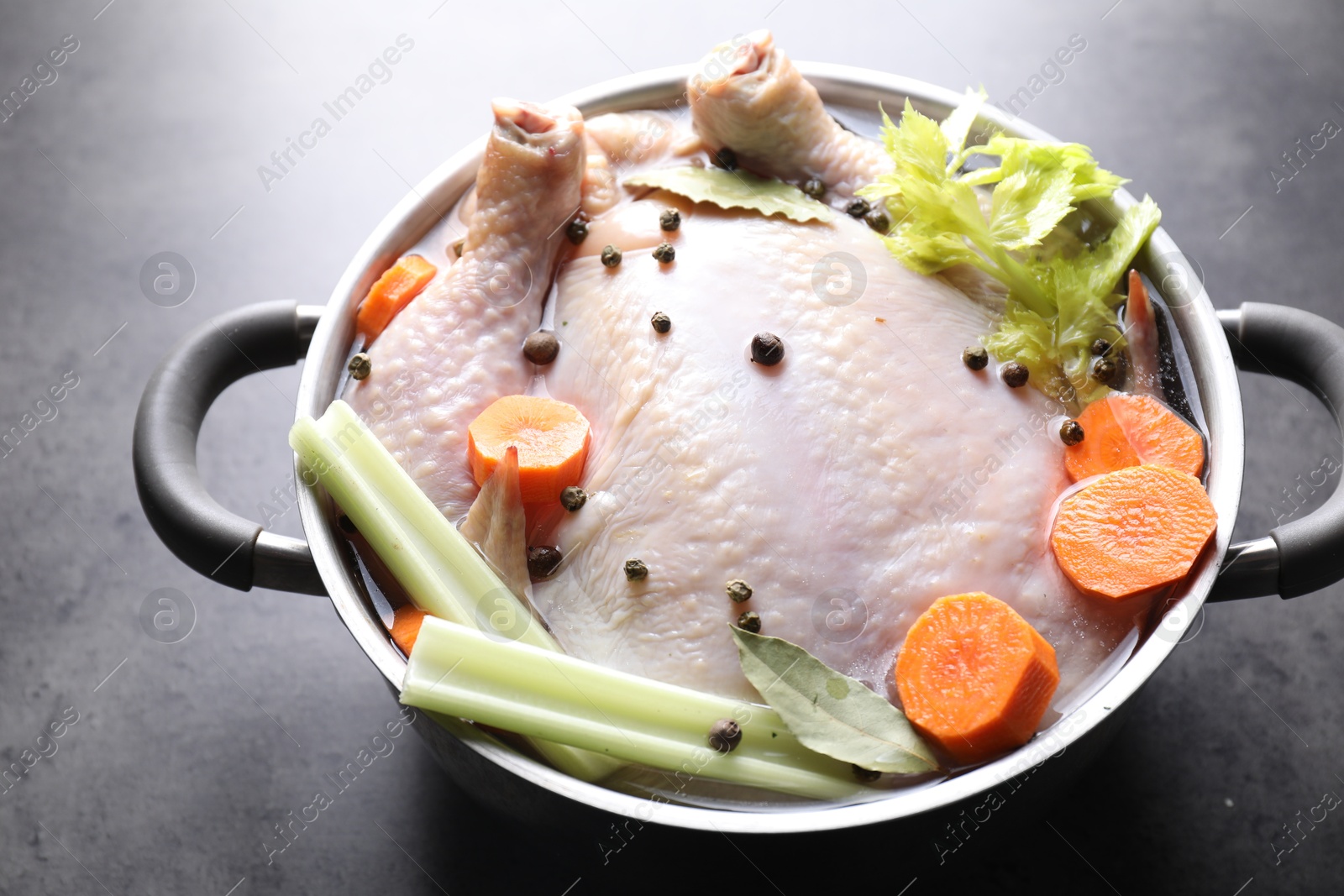 Photo of Whole raw turkey, cut carrot, celery and spices in pot on grey textured table, closeup