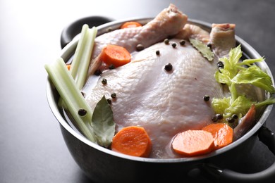 Photo of Whole raw turkey, cut carrot, celery and spices in pot on grey table, closeup