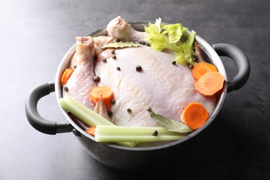 Photo of Whole raw turkey, cut carrot, celery and spices in pot on grey table, closeup