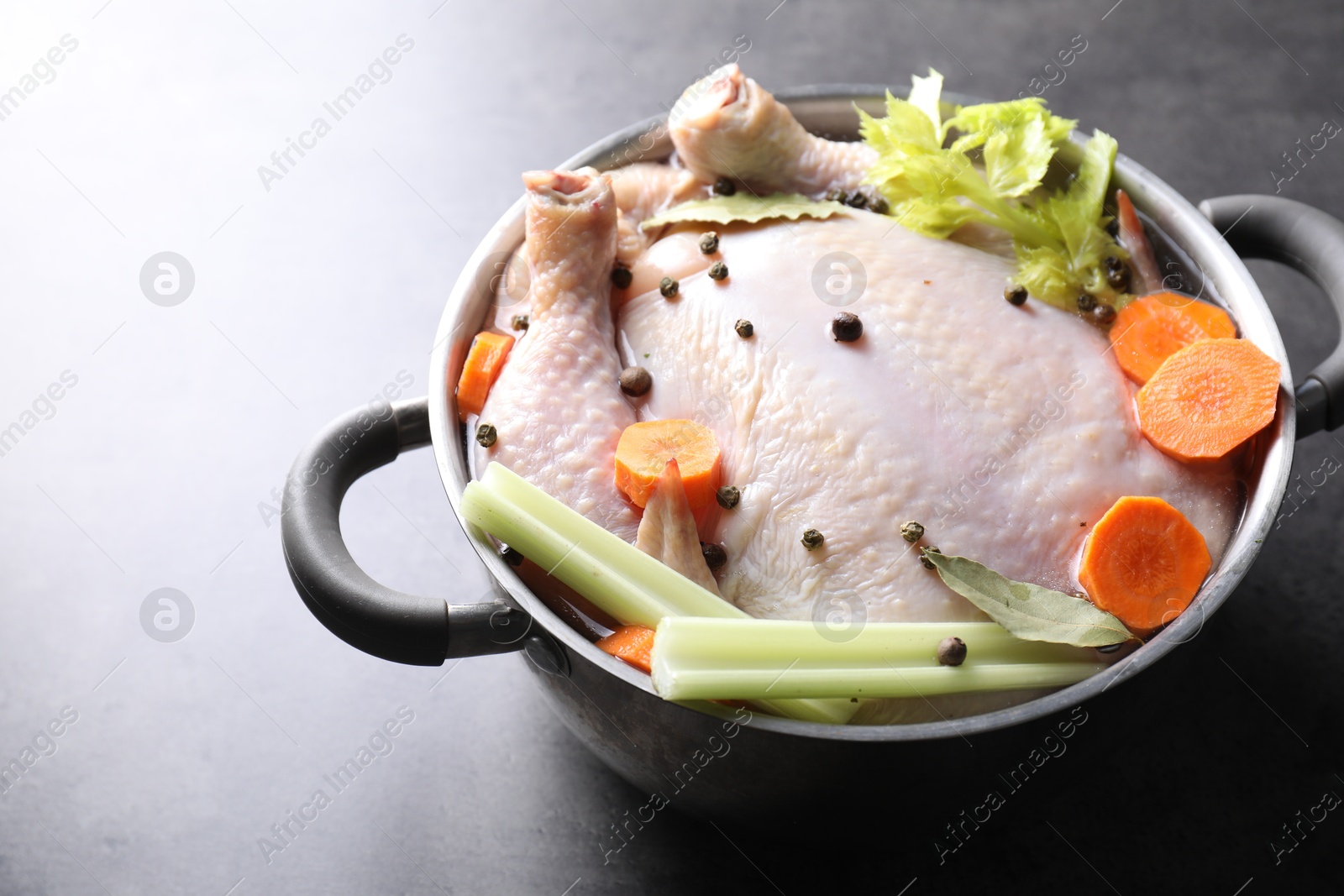 Photo of Whole raw turkey, cut carrot, celery and spices in pot on grey table, closeup