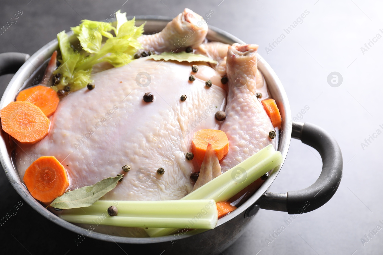 Photo of Whole raw turkey, cut carrot, celery and spices in pot on grey table, closeup