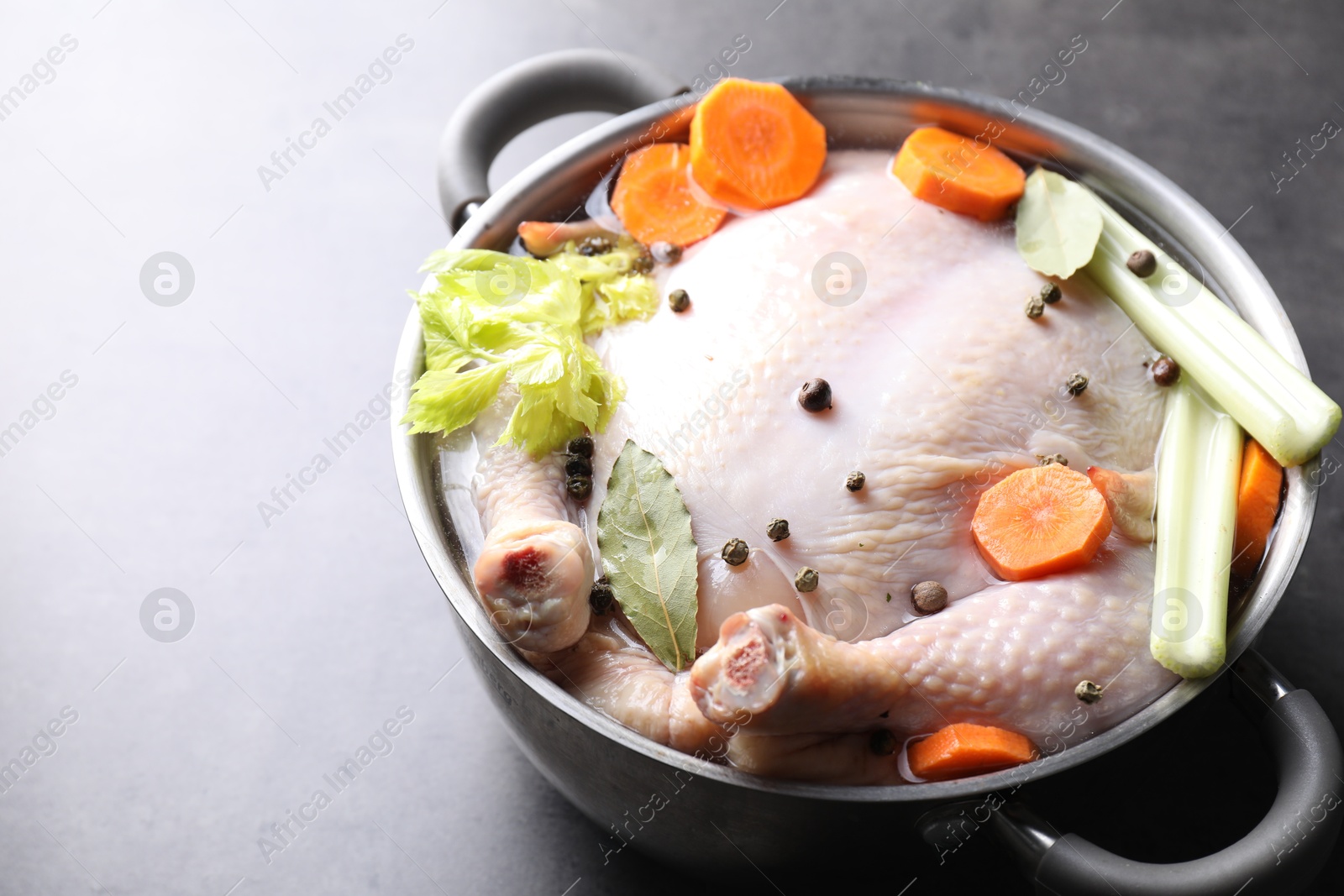 Photo of Whole raw turkey, cut carrot, celery and spices in pot on grey textured table, closeup. Space for text