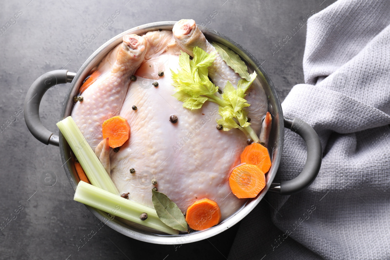 Photo of Whole raw turkey, cut carrot, celery and spices in pot on grey textured table, top view