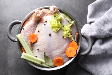 Photo of Whole raw turkey, cut carrot, celery and spices in pot on grey textured table, top view