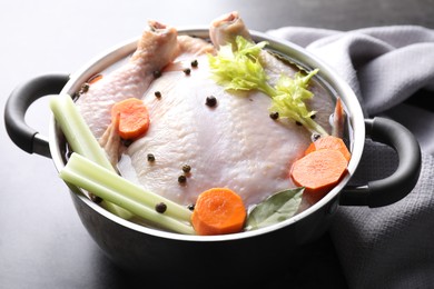 Photo of Whole raw turkey, cut carrot, celery and spices in pot on grey table, closeup