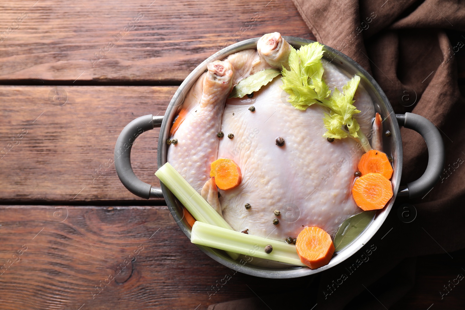 Photo of Whole raw turkey, cut carrot, celery and spices in pot on wooden table, top view. Space for text