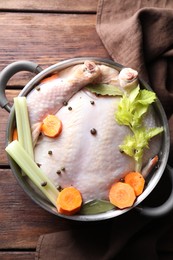 Photo of Whole raw turkey, cut carrot, celery and spices in pot on wooden table, top view