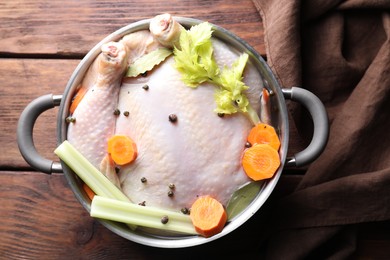 Photo of Whole raw turkey, cut carrot, celery and spices in pot on wooden table, top view